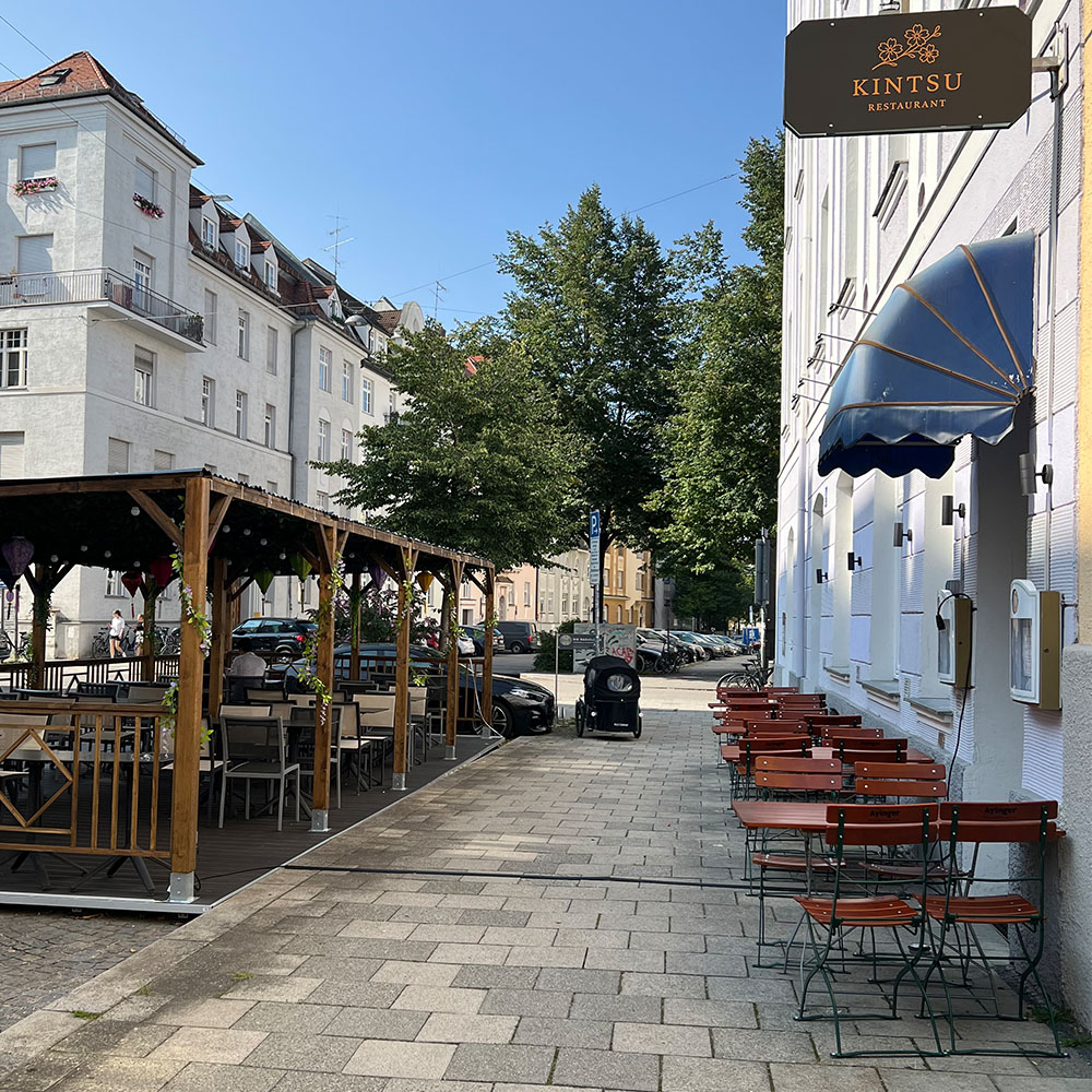 Eine leere Restaurantterrasse mit Holzbänken und Sonnenschirmen im Freien.