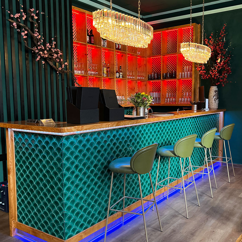 Ein stilvoller moderner Barbereich mit grüner Theke, roten Regalen und eleganten Kronleuchtern.