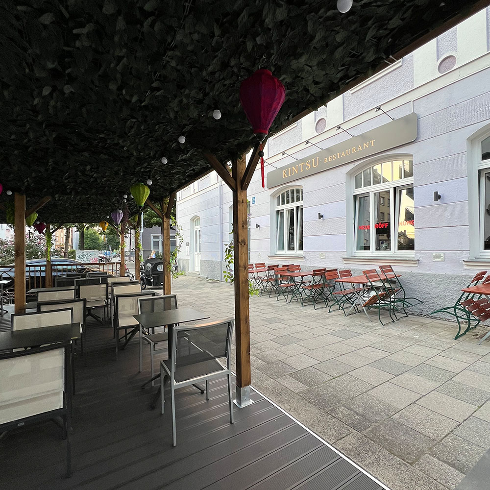 Überdachte Terrasse eines Restaurants mit Holzmöbeln und dekorativen Laternen.