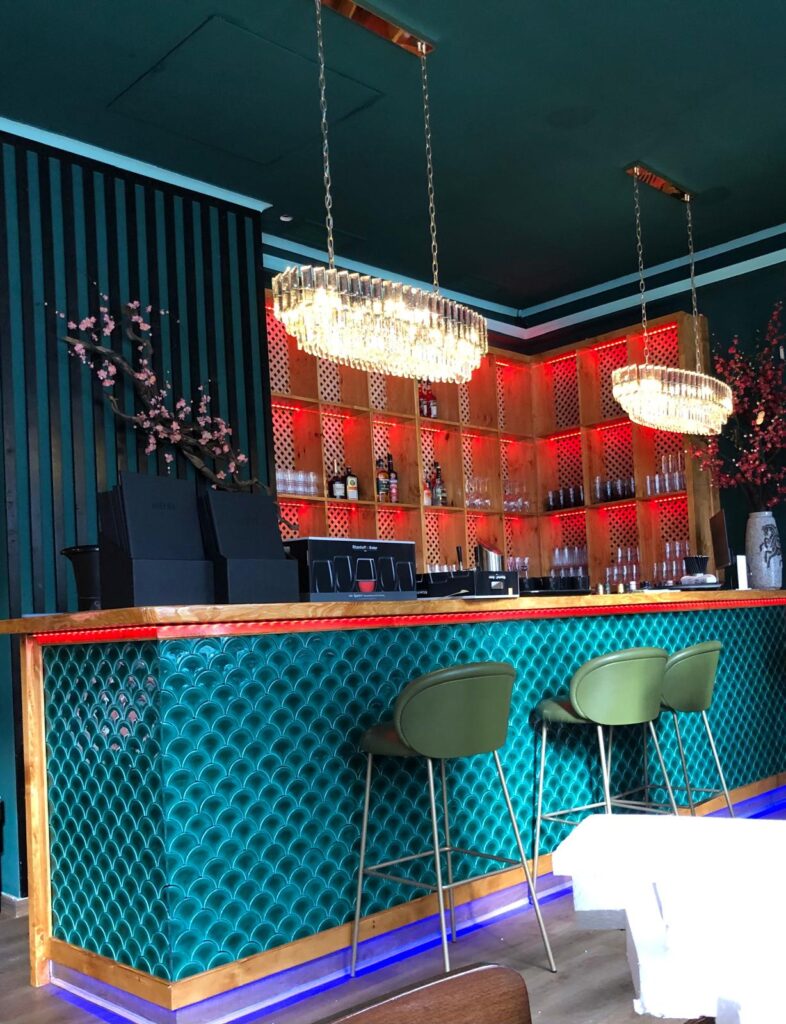 Elegante Bar mit grüner Wellendecke, roten Lichtern und Kristallleuchtern.
