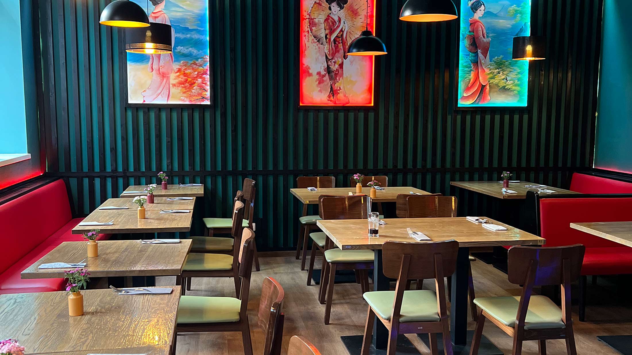 Ein gemütliches Restaurant mit Holztischen, roten und grünen Akzenten und leuchtenden Bildern an der Wand.