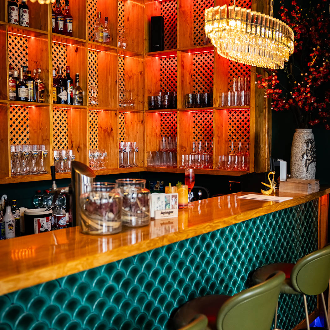 Eine stilvolle Bar mit grüner Theke, goldfarbenen Akzenten und leuchtenden Regalen