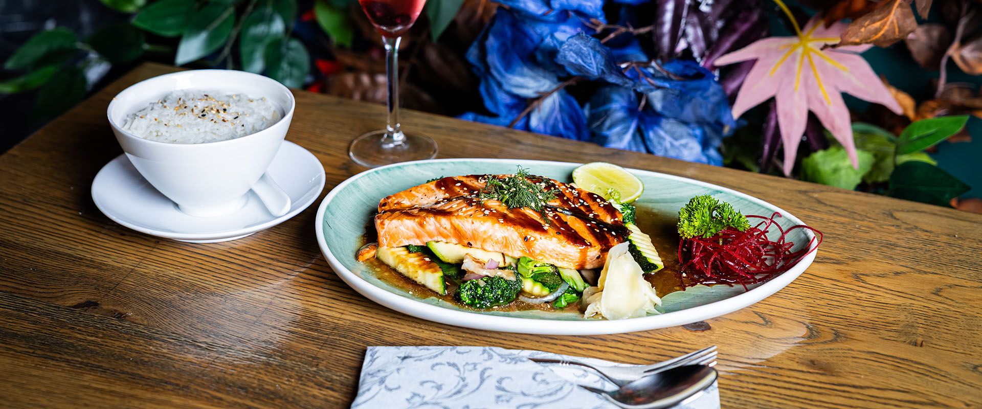 Gegrillter Lachs mit Gemüse und Limette auf einem Teller, dazu eine Schale Reis