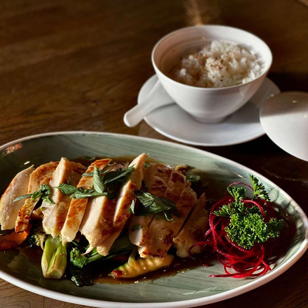 Ein grüner Teller mit gebratenem Hähnchen, Gemüse und Kräutern.