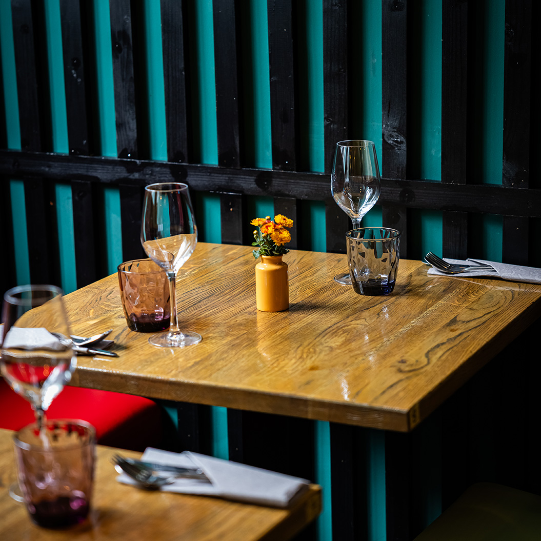 Ein leerer Holztisch mit Gläsern, Besteck und einer kleinen gelben Blumenvase