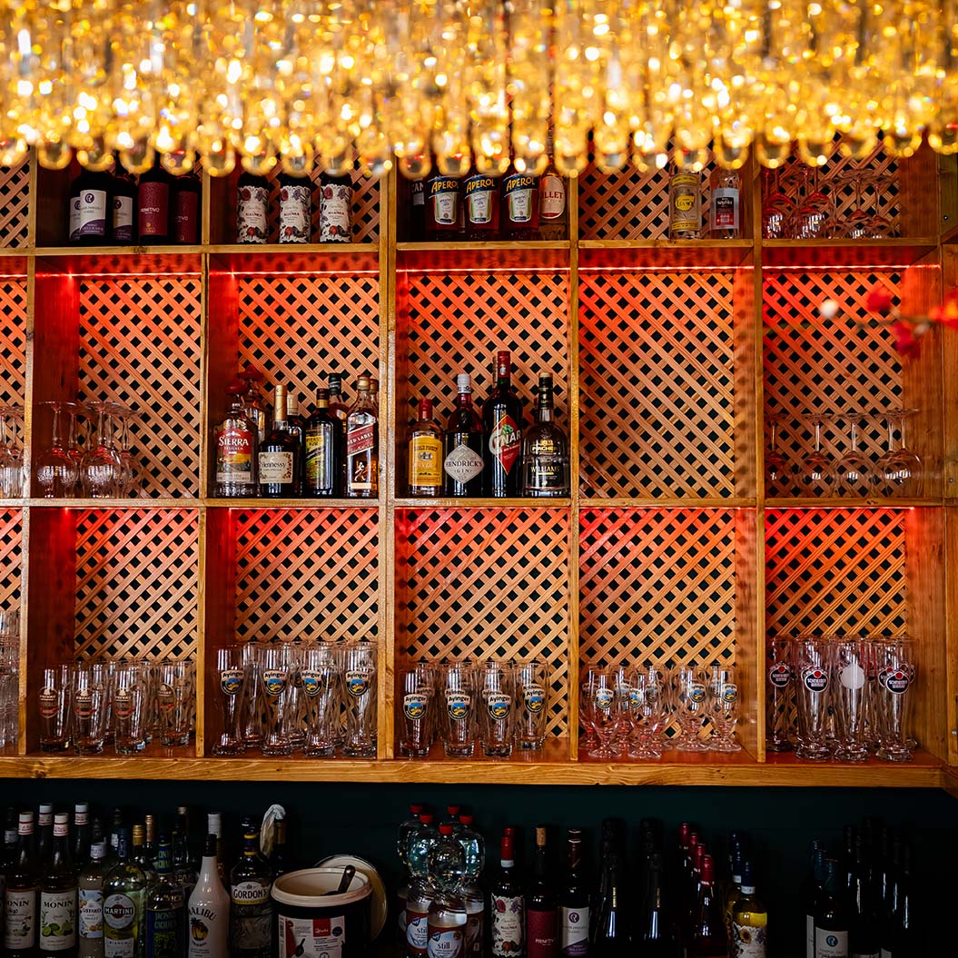 Flaschen und Gläser stehen vor einem beleuchteten Holzgitterregal und funkelndem Glas