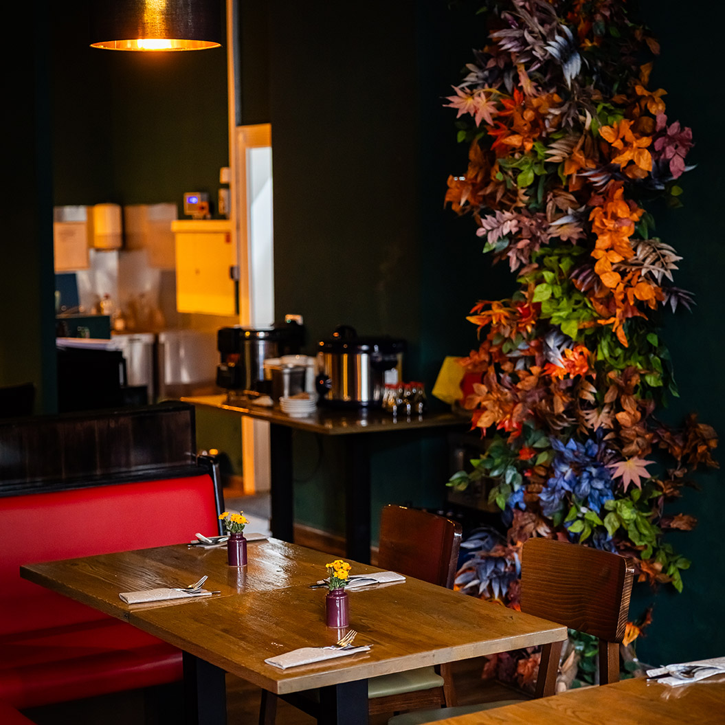 Gemütliches Restaurant mit Holztischen, roter Bank und bunter Blätterdekoration