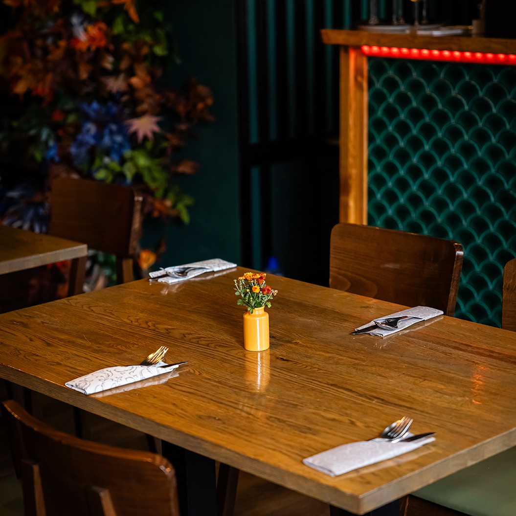 Ein leerer Holztisch mit vier Gedecken und einer gelben Blumenvase in der Mitte