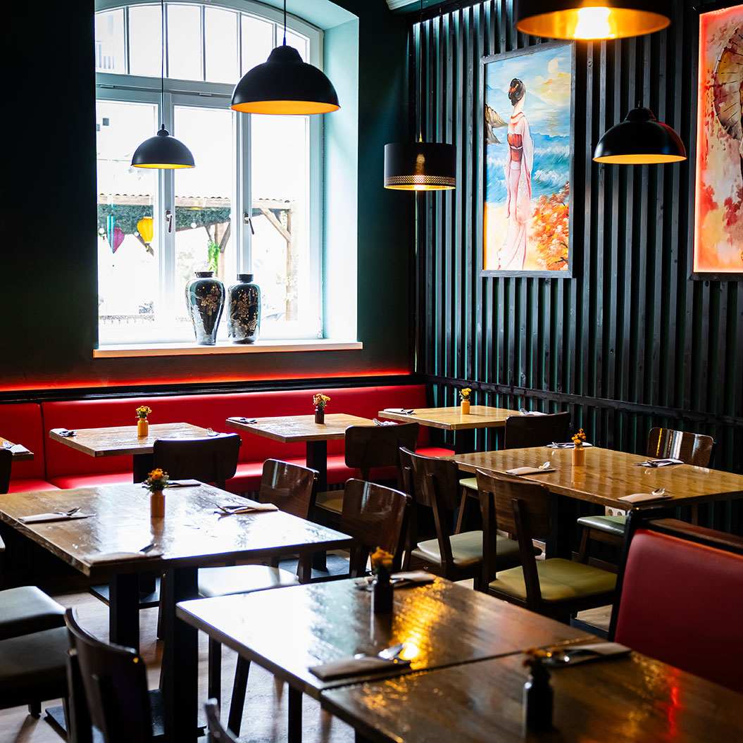 Ein modernes Restaurant mit Holztischen, roter Polsterbank und japanischer Kunst