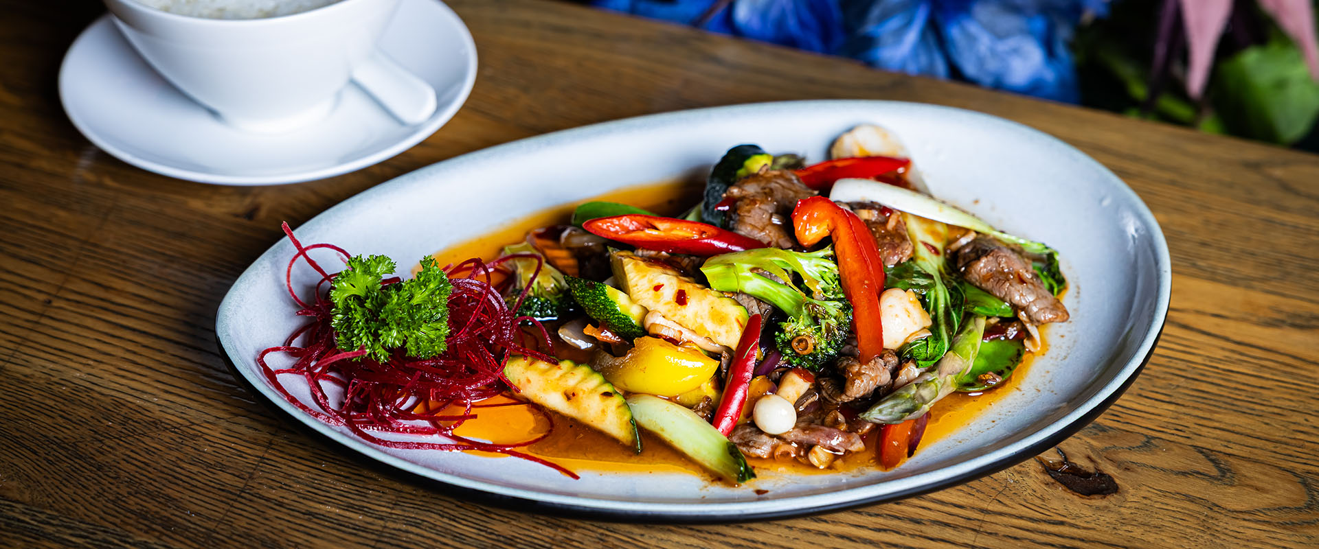 Ein bunt angerichtetes asiatisches Gemüsegericht mit Fleisch, Chili und Reis auf einem weißen Teller