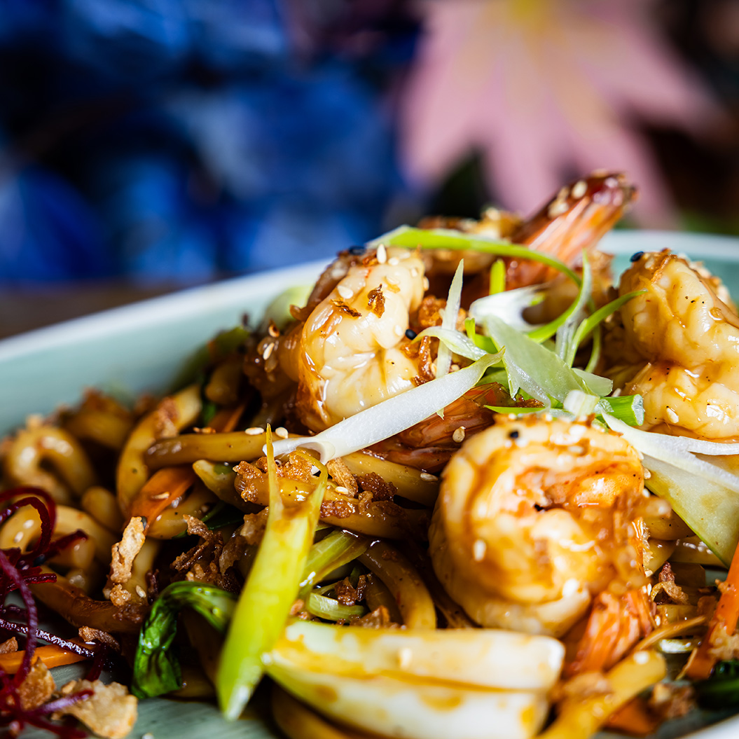 Ein Teller mit braun gebratenen Garnelen, gebratenen Nudeln und grünem Gemüse