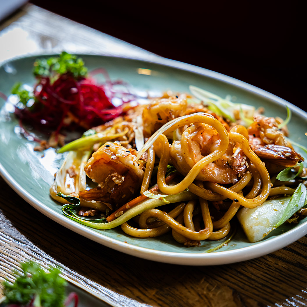 Ein Teller mit glänzenden braunen Nudeln, Garnelen, frischem Gemüse und roten Rüben